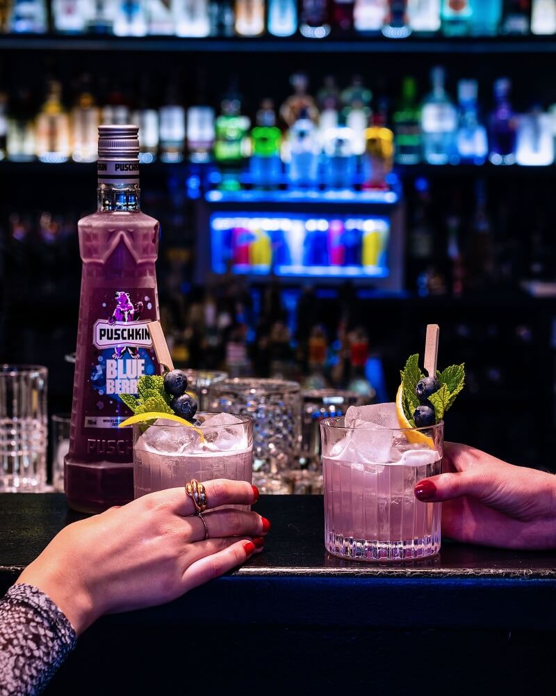 Zwei Personen stoßen in einer Bar mit Puschkin Blueberry Gläsern an